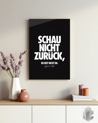 Motivationsposter mit dem Zitat ‚Schau nicht zurück, du bist nicht da‘ in weißer Typografie auf schwarzem Hintergrund, das den Fokus auf die Zukunft legt.